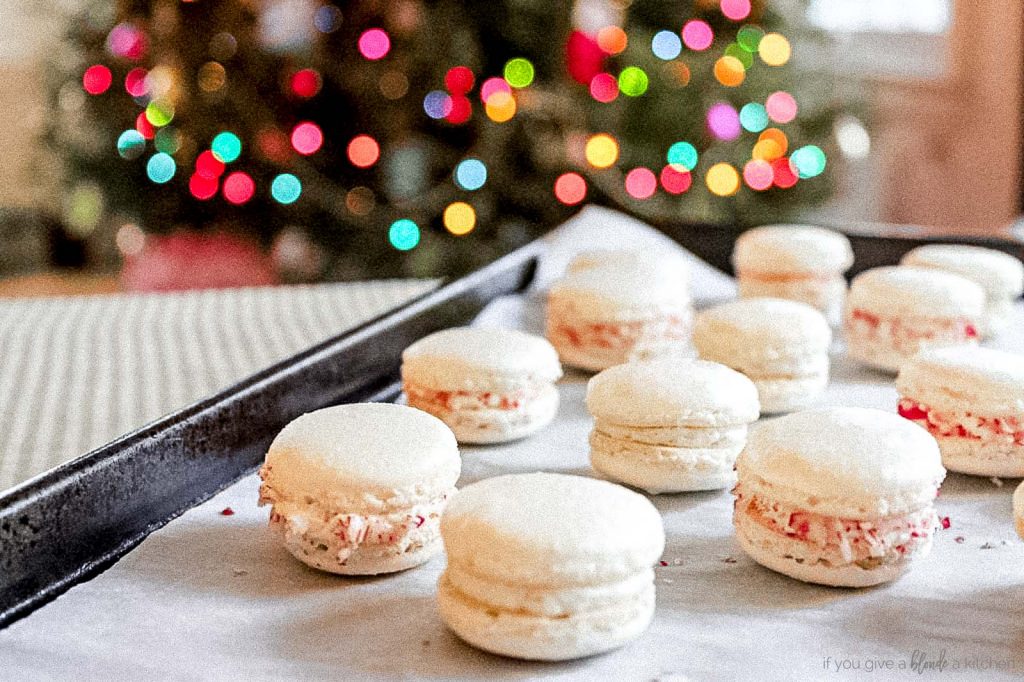 christmas macarons on baking sheet with christmas lights on tree