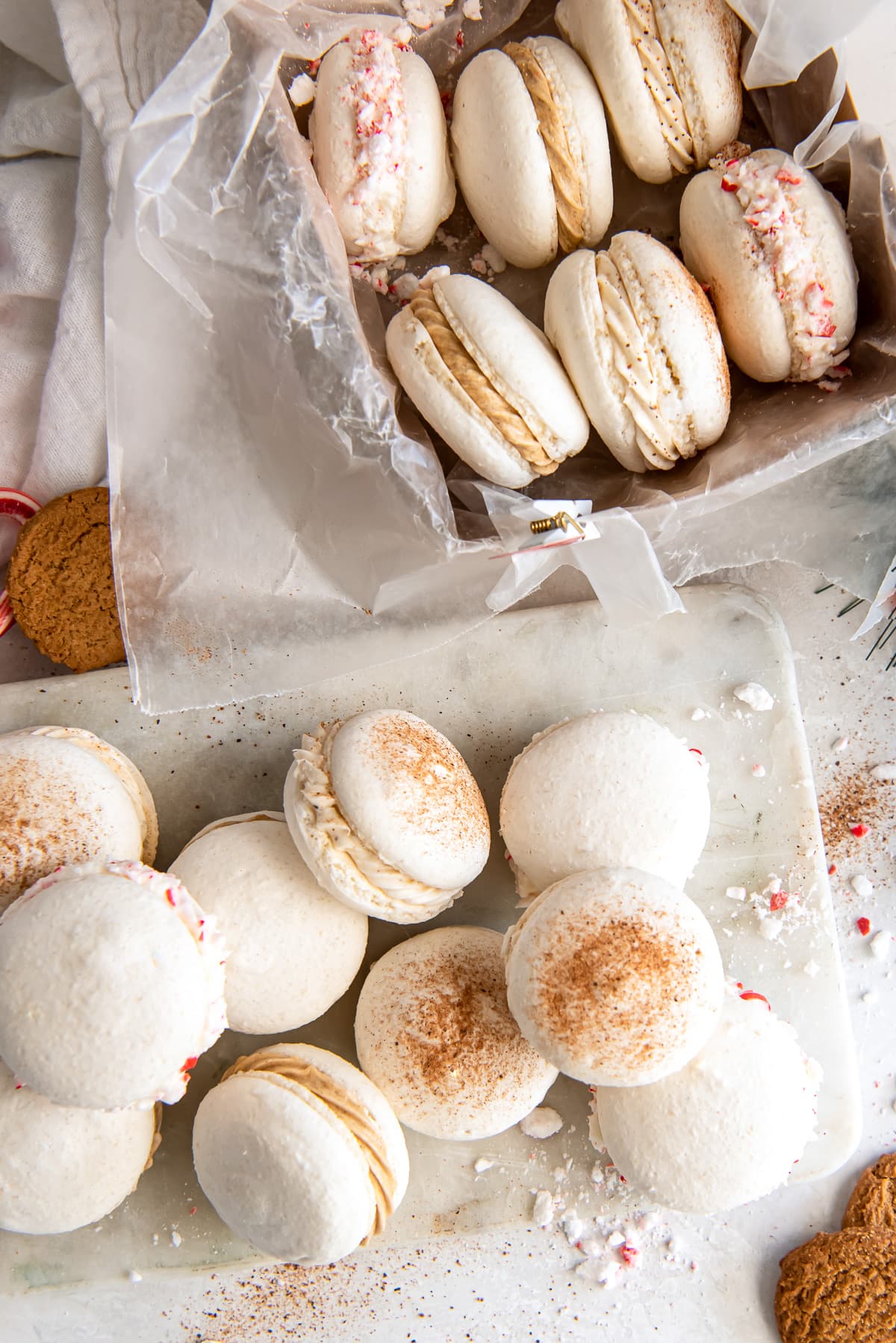 christmas macarons in a pile on marble next to more macarons in a cookie box.