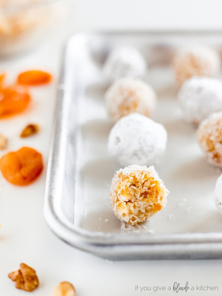 coconut apricot ball with bite sitting on parchment lined baking sheet