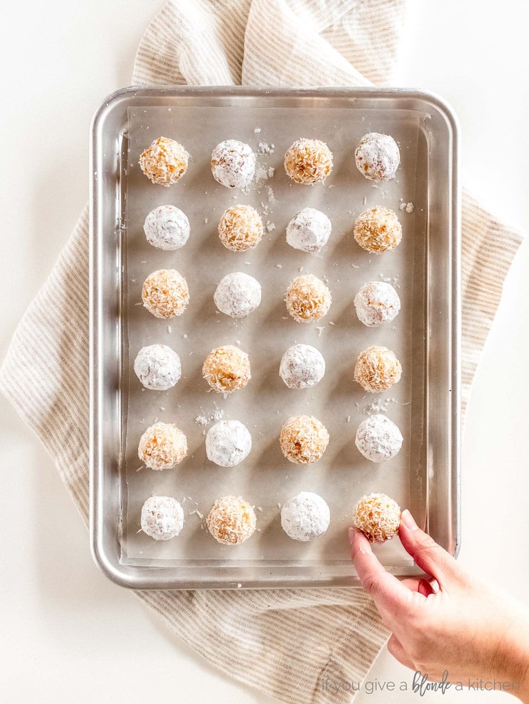 hand reaching for coconut apricot ball on baking pan