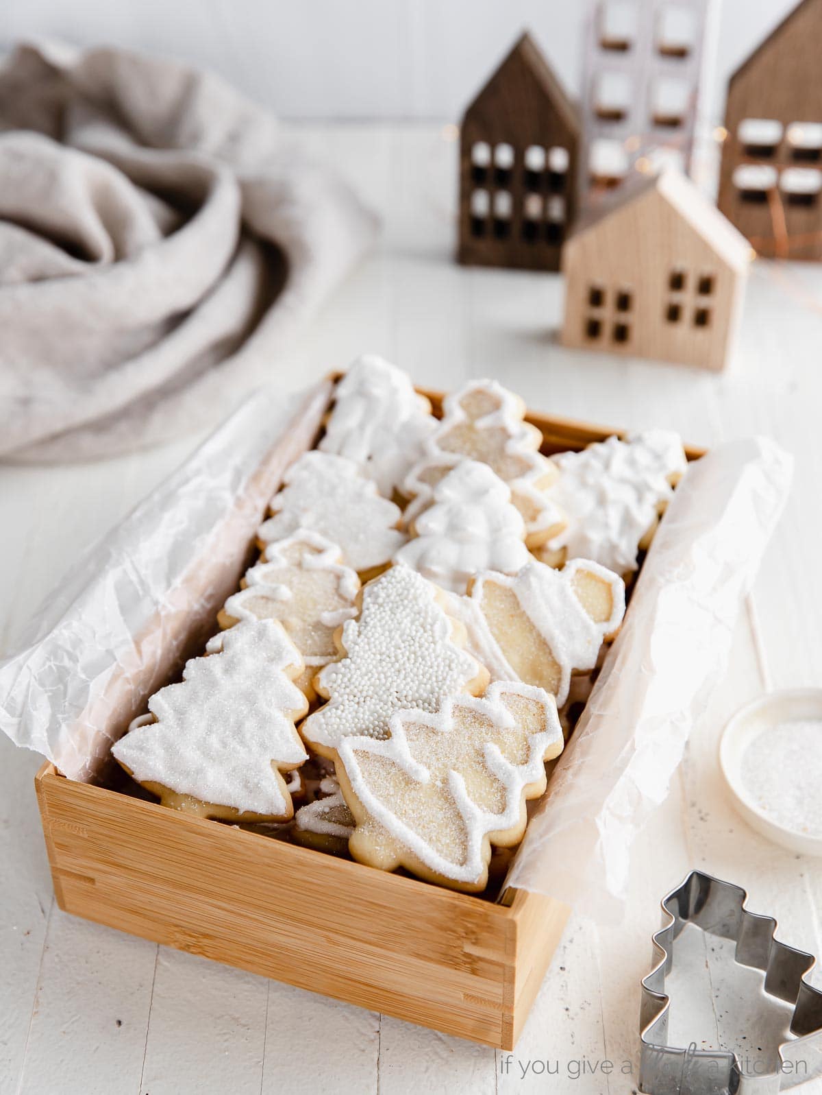 iced christmas tree sugar cookies in a wooden box. brown wooden houses behind box