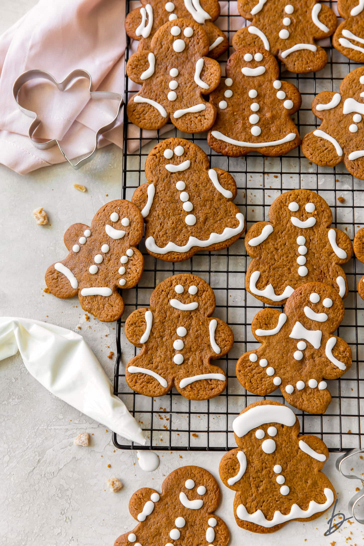 iced gingerbread man cookies on wire cooling rack next to pink kitchen cloth and icing bag with royal icing