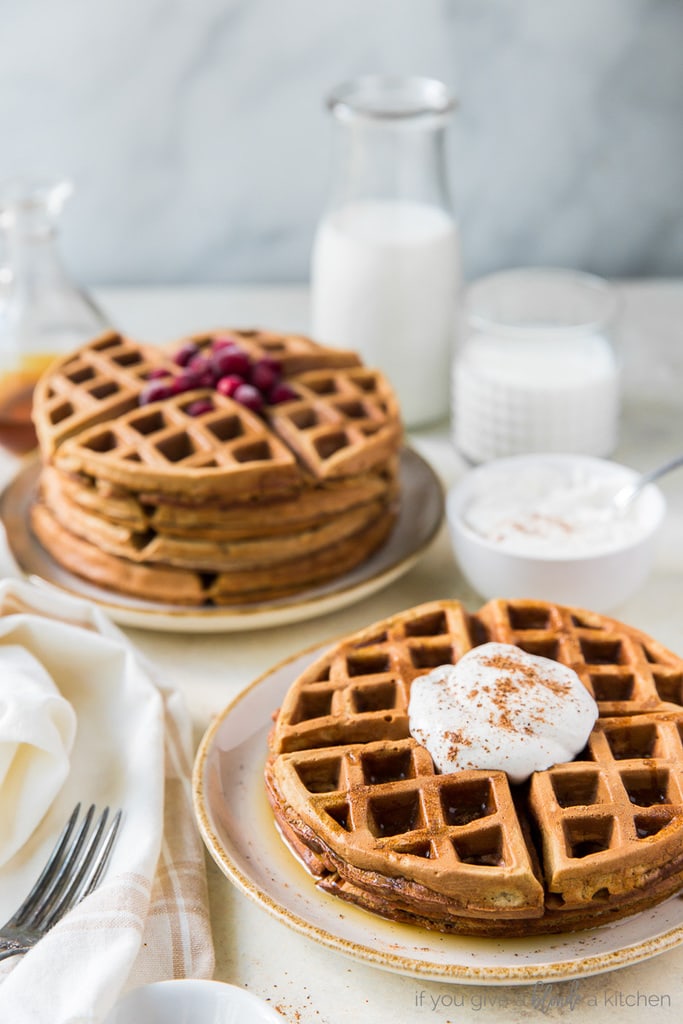 gingerbread waffles on plates. One stack topped with eggnog whipped cream; milk bottle behind plates