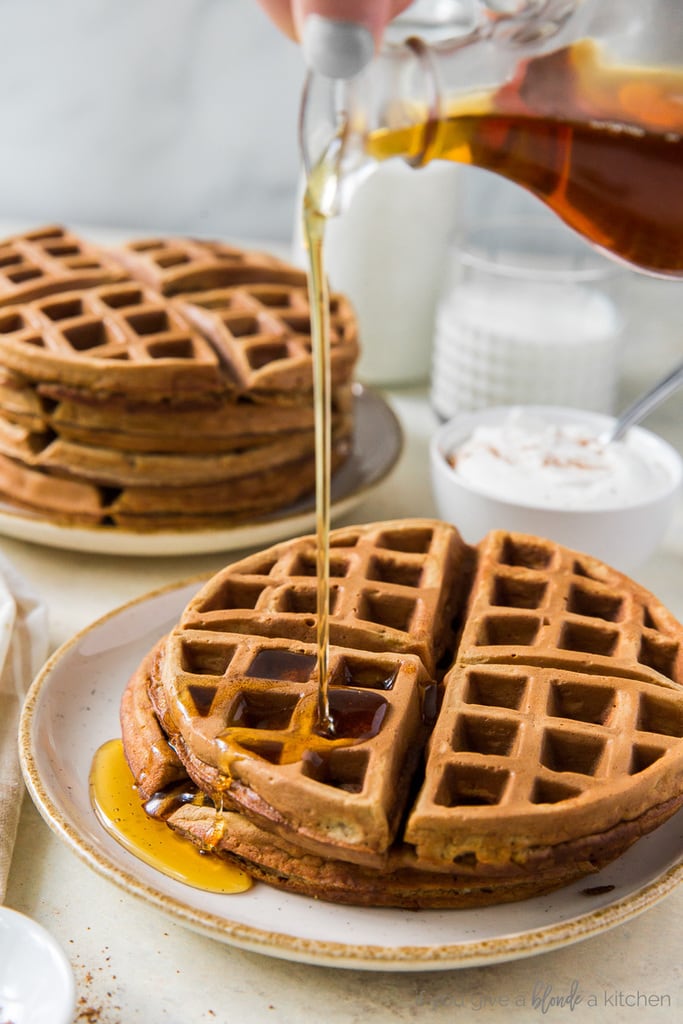 hand holden glass pitcher pouring maple syrup over gingerbread waffles