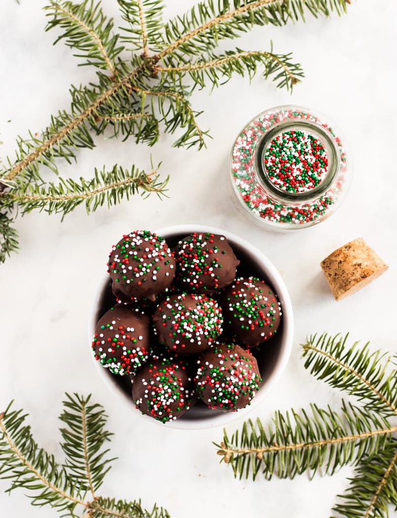 chocolate covered peanut butter balls in white bowl. Glass jar of red and green sprinkles