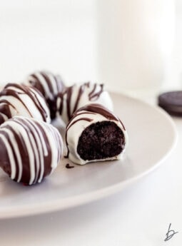 white chocolate covered oreo truffle with a bite on a plate with more truffles.