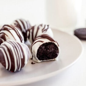 white chocolate covered oreo truffle with a bite on a plate with more truffles.
