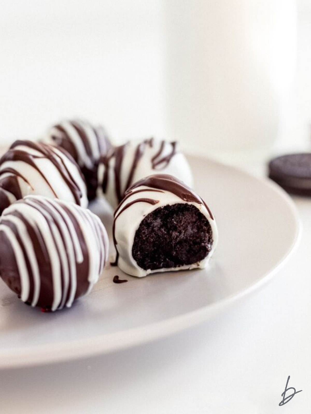 white chocolate covered oreo truffle with a bite on a plate with more truffles.