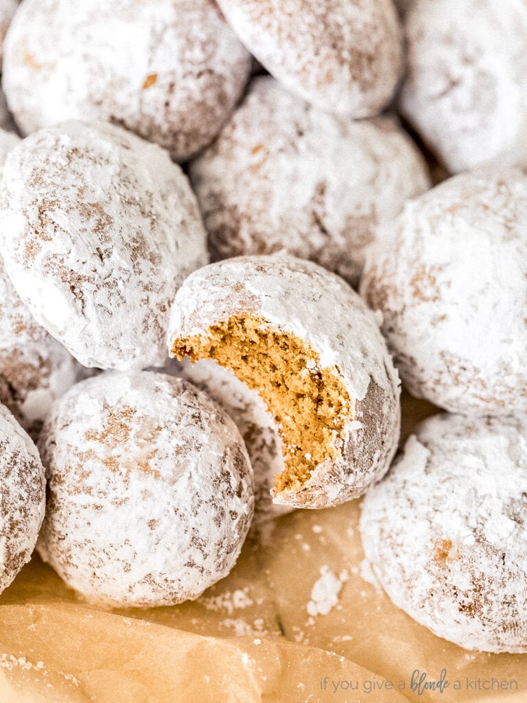 pile of pfeffernusse cookies coated in confectioners' sugar. One cookie with bite