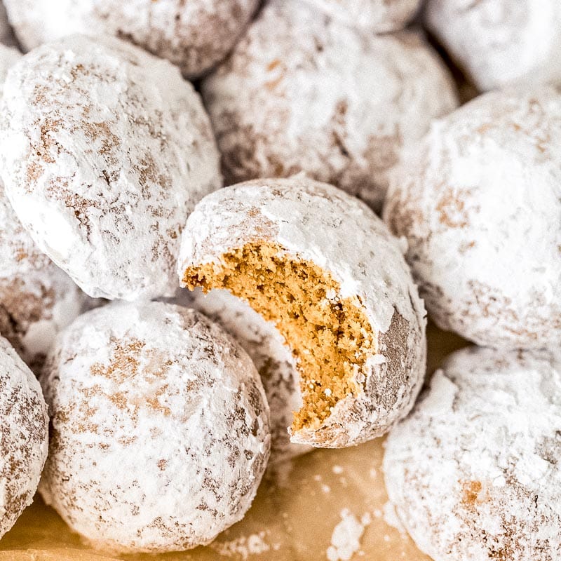 pfeffernusse cookies coated in confectioners' sugar. one cookie with a bite