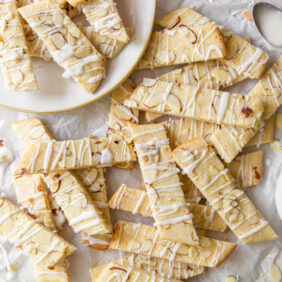 scandinavian almond bars topped with drizzle and slivered almonds in a pile on crinkled parchment paper.