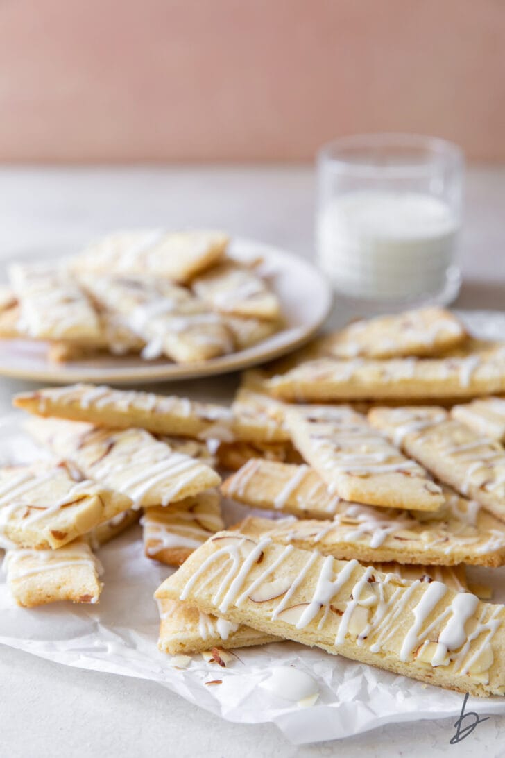 scandinavian almond bars in a pile in front of plate of more bars and glass of milk