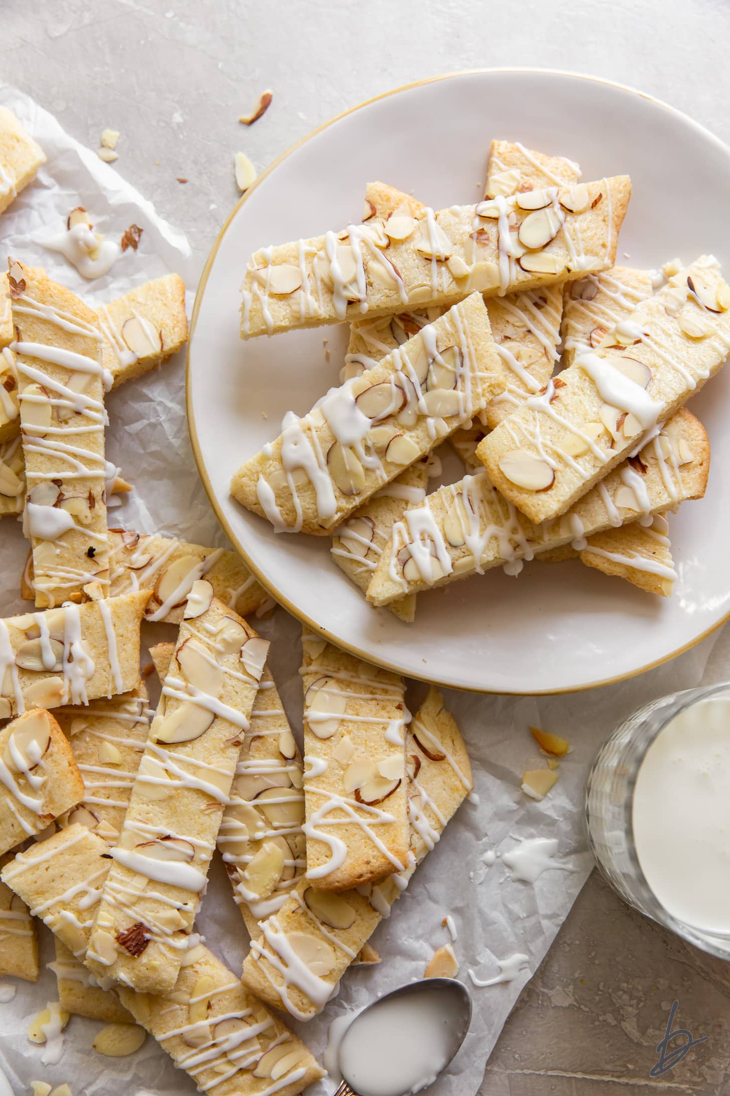 plate of scandinavian almond bars next to more bars on parchment paper and glass of milk.