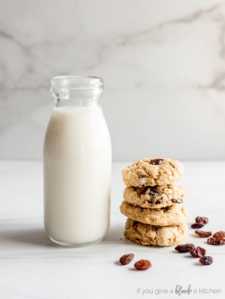 stack of four oatmeal raisin cookies next to glass bottle of milk