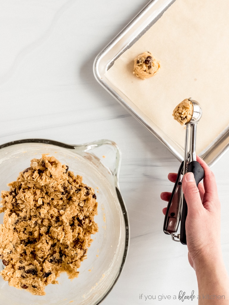 hand spooning oatmeal raisin cookie dough onto parchment lined baking sheet