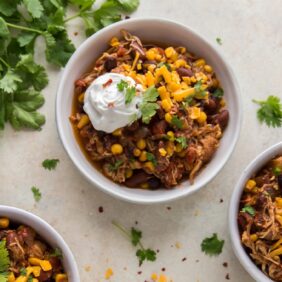 crock pot chicken chili in bowls topped with sour cream and cheese