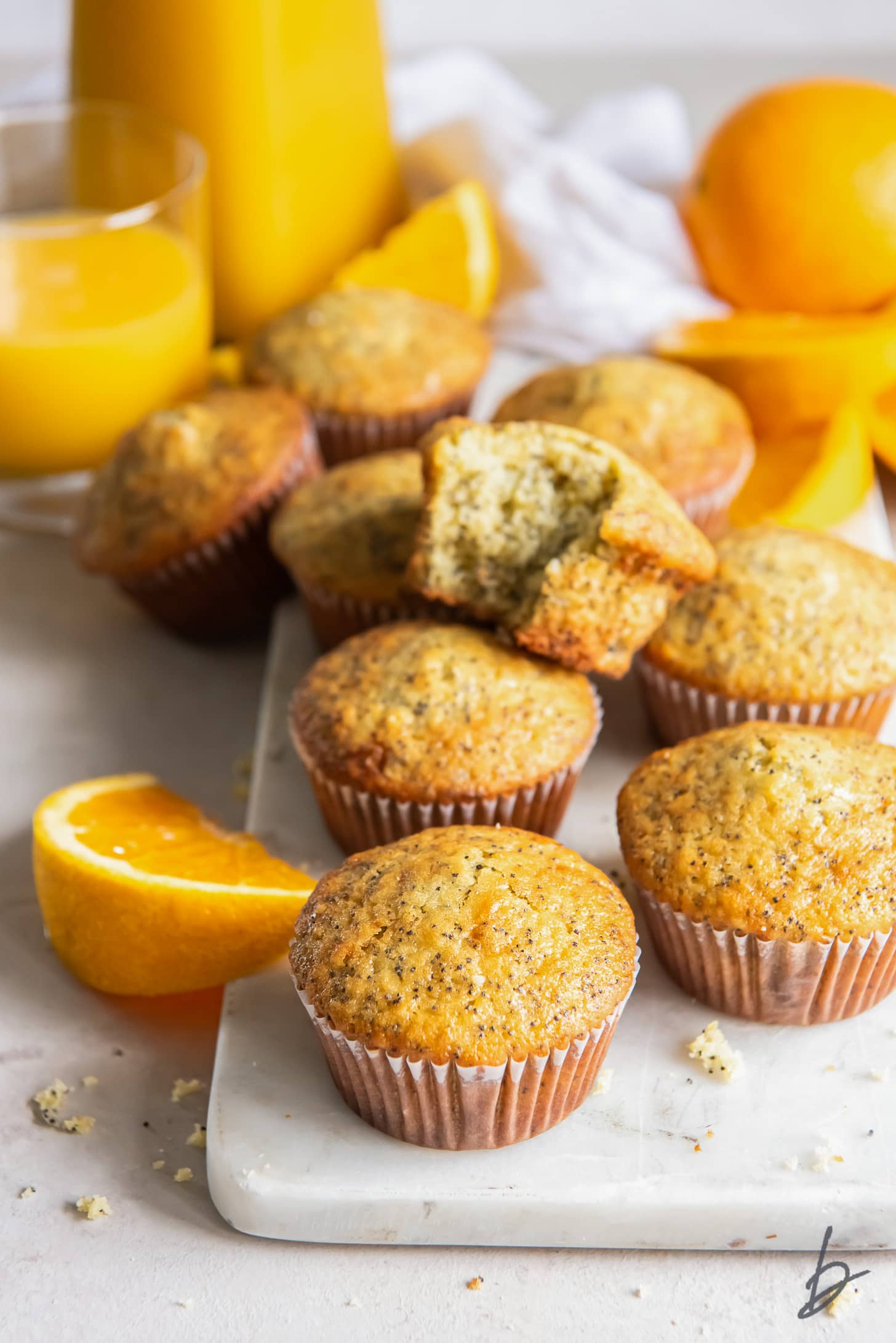 Orange poppy seed muffins on a marble slab next to oranges and orange slices