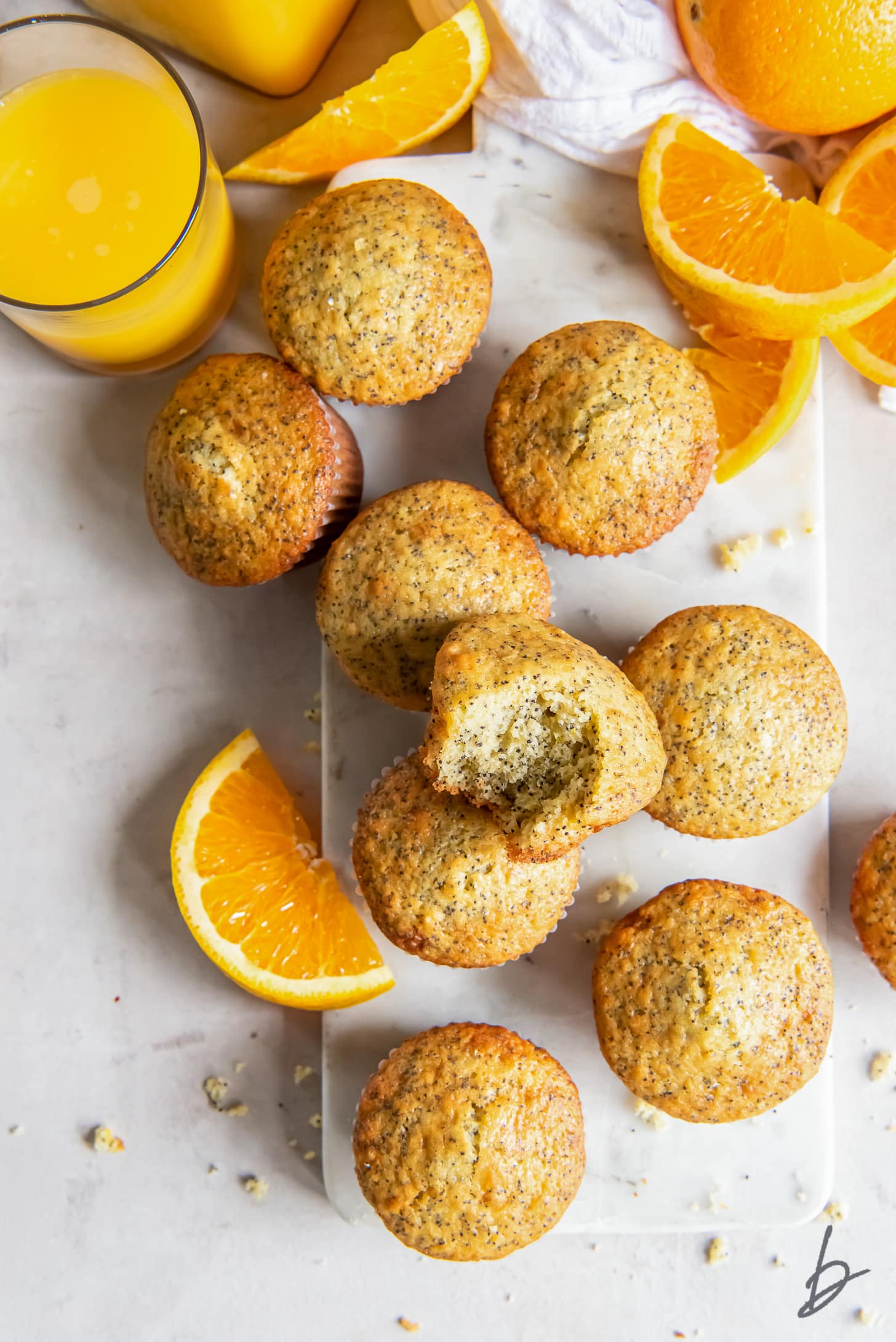 orange poppy seed muffins with one muffin with a bite on a marble slab next to orange slices