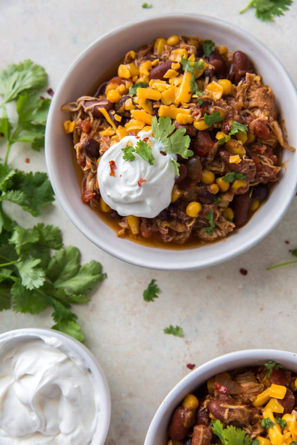 chicken chili topped with shredded cheese and sour cream in a white bowl
