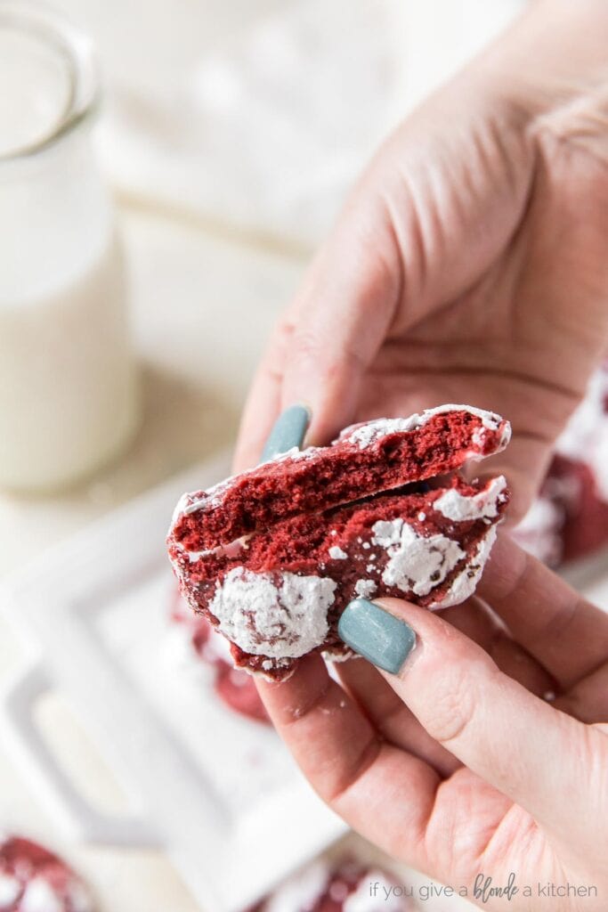 Hands breaking red velvet crinkle cookie in half to show chewy center