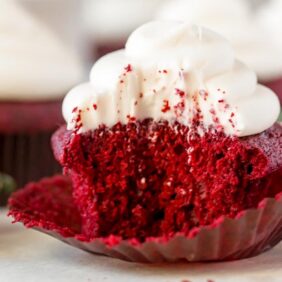 red velvet cupcake with cream cheese frosting and a bite next to fresh strawberries