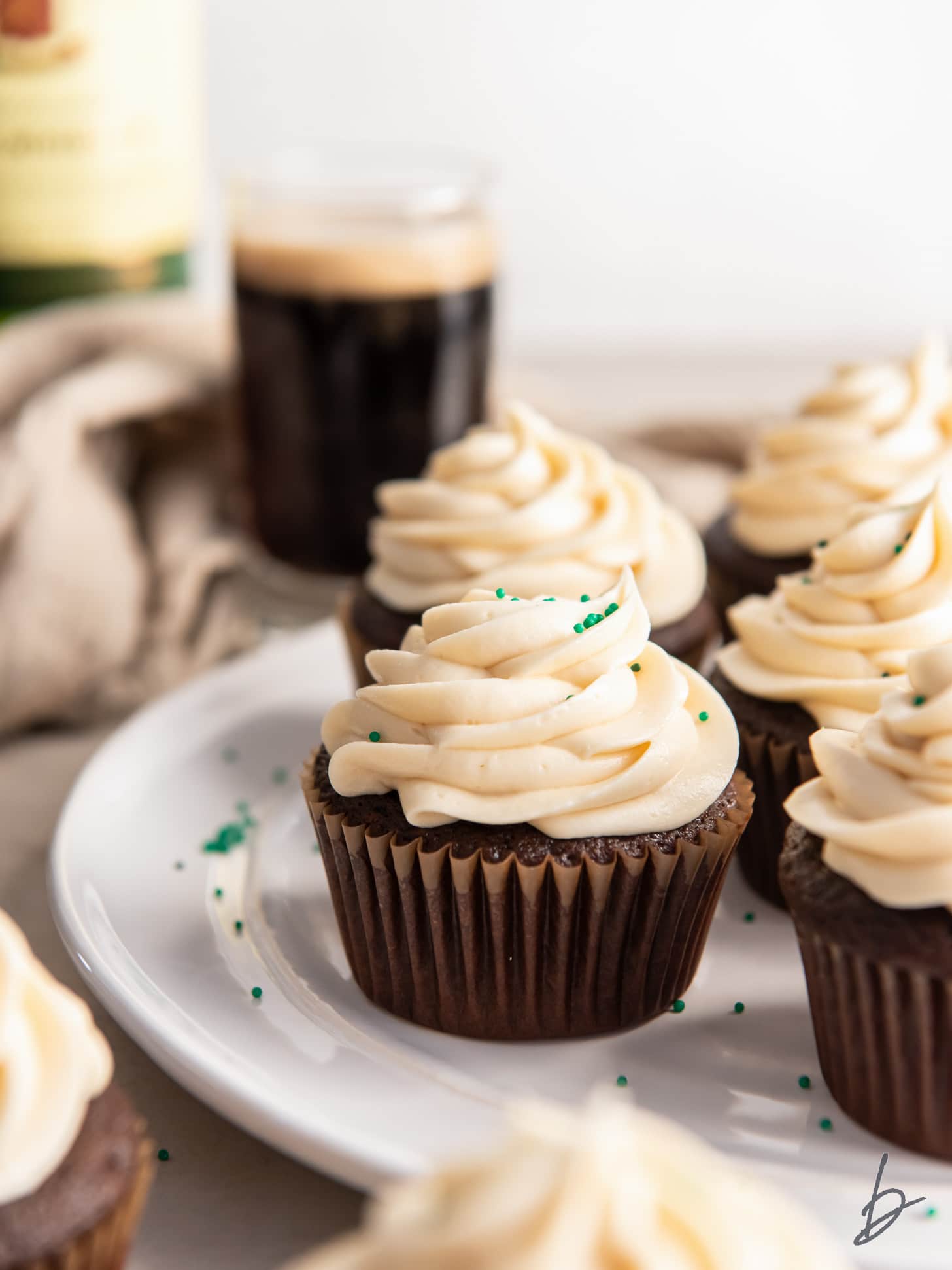 guinness cupcakes with baileys frosting on a plate with a few green sprinkles.