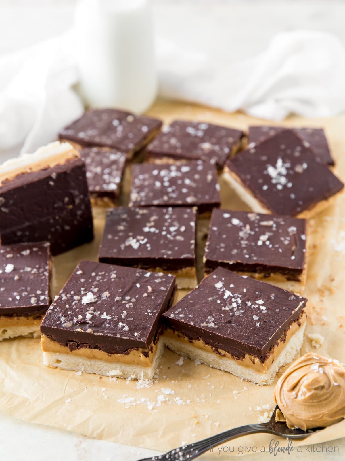 peanut butter chocolate bars with sea salt on parchment paper with spoon of peanut butter