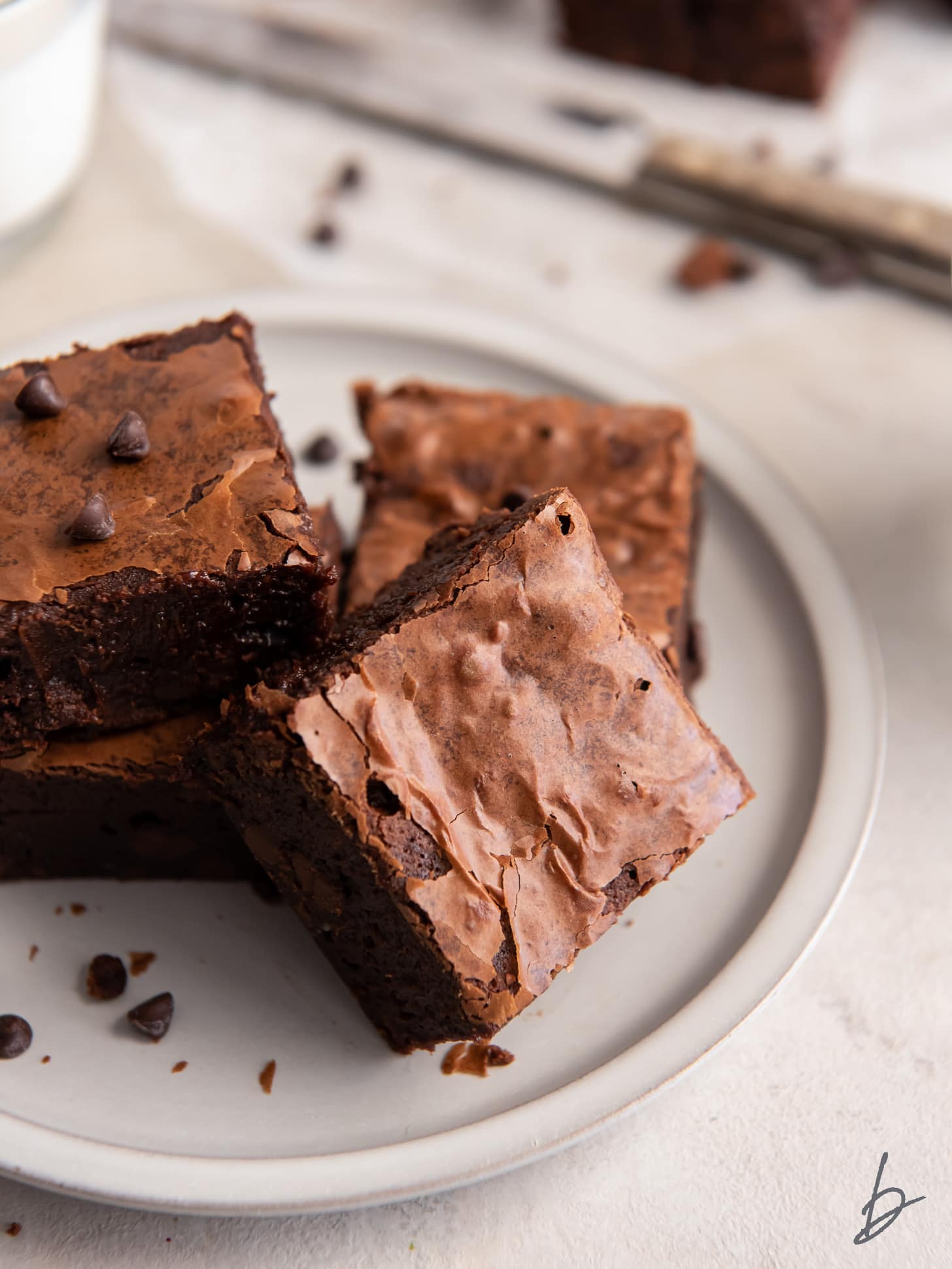 homemade brownie with shiny top on a plate leaning again a few more brownies.