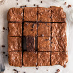 brownie on its side next to more brownies cut into squares on parchment paper.