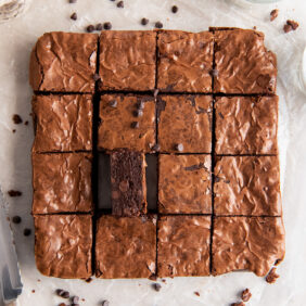 brownie on its side next to more brownies cut into squares on parchment paper.