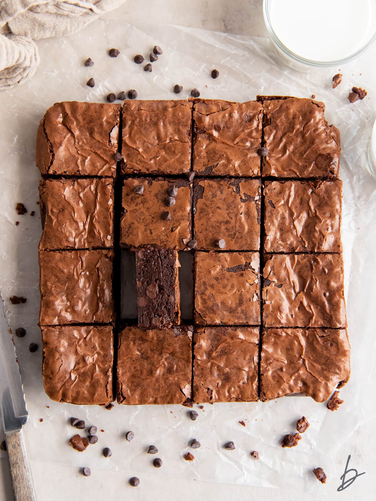 brownie on its side next to more brownies cut into squares on parchment paper.