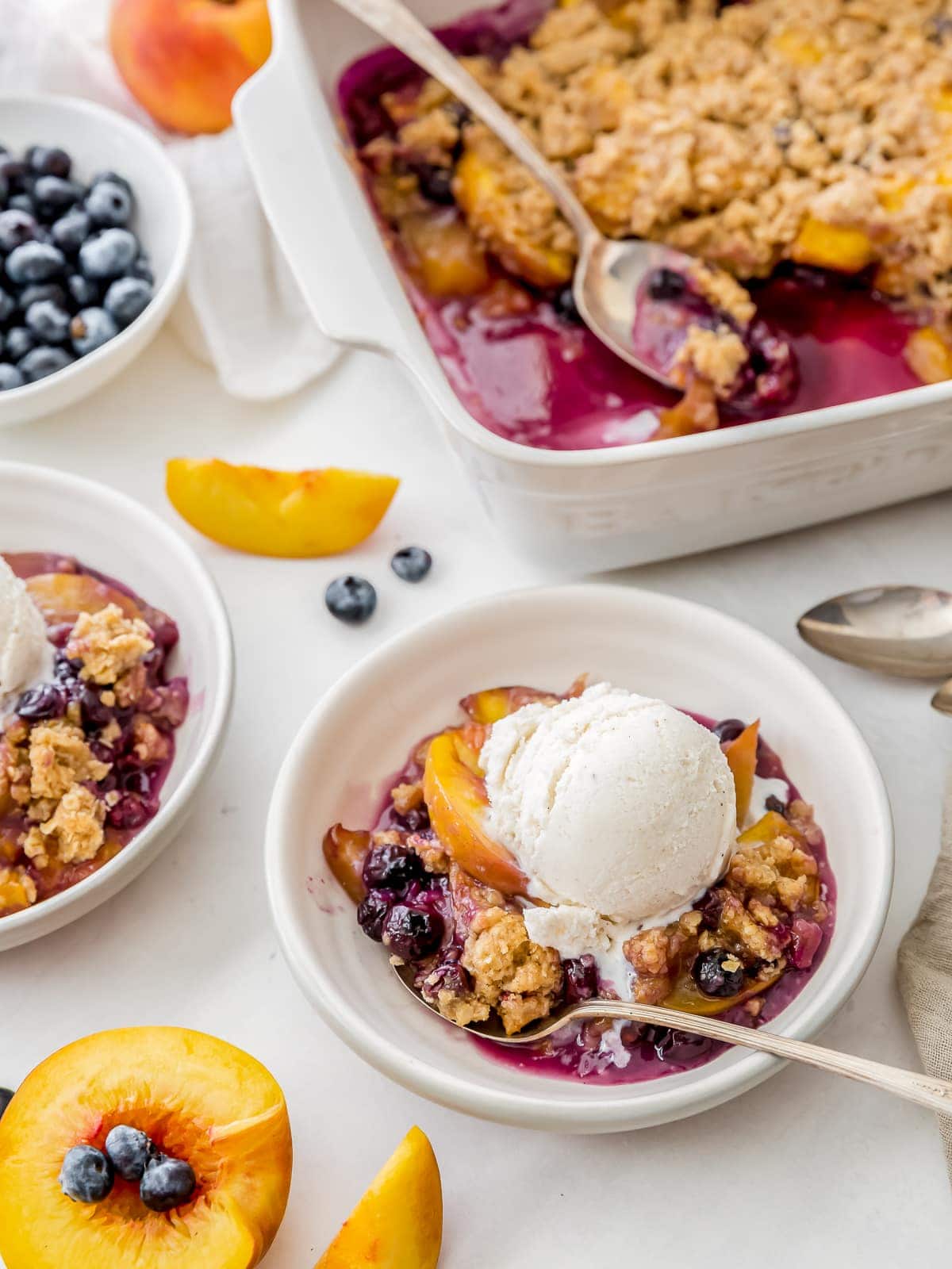 peach blueberry crisp in a bowl with scoop of vanilla ice cream