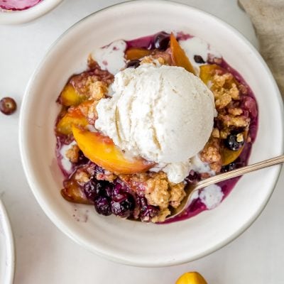 bowl of peach blueberry crisp with scoop of vanilla ice cream.