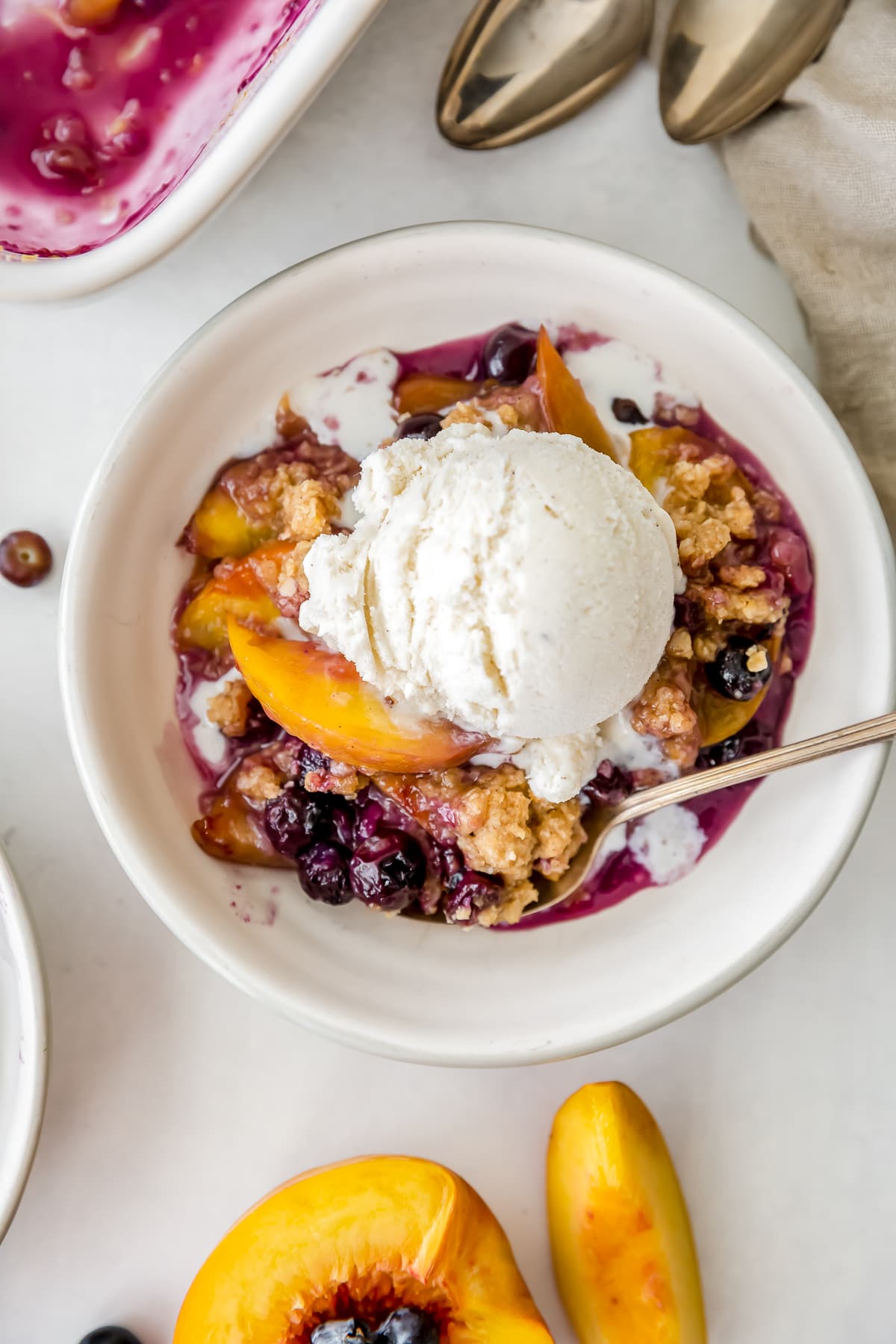 bowl of peach blueberry crisp with scoop of vanilla ice cream