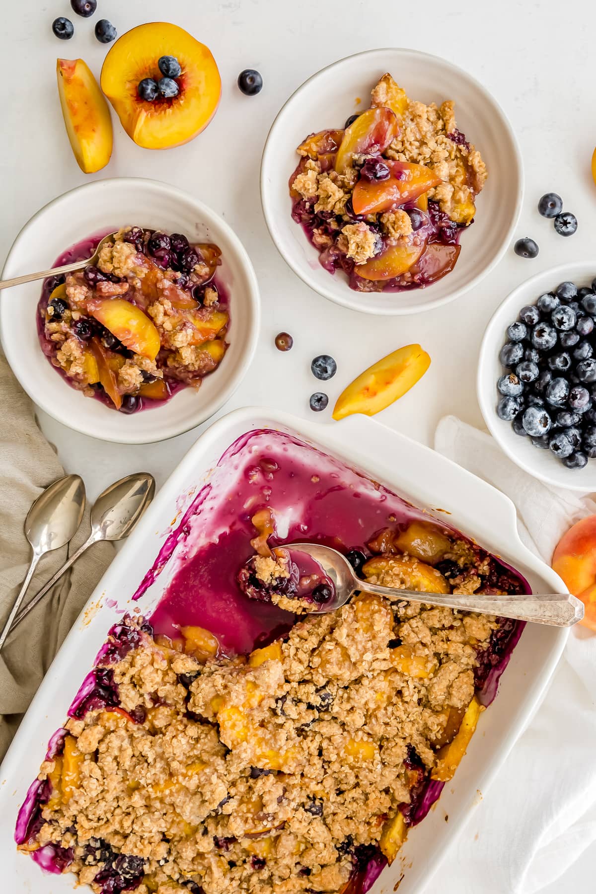 peach blueberry crisp in a baking dish and two servings in bowls next to the baking dish