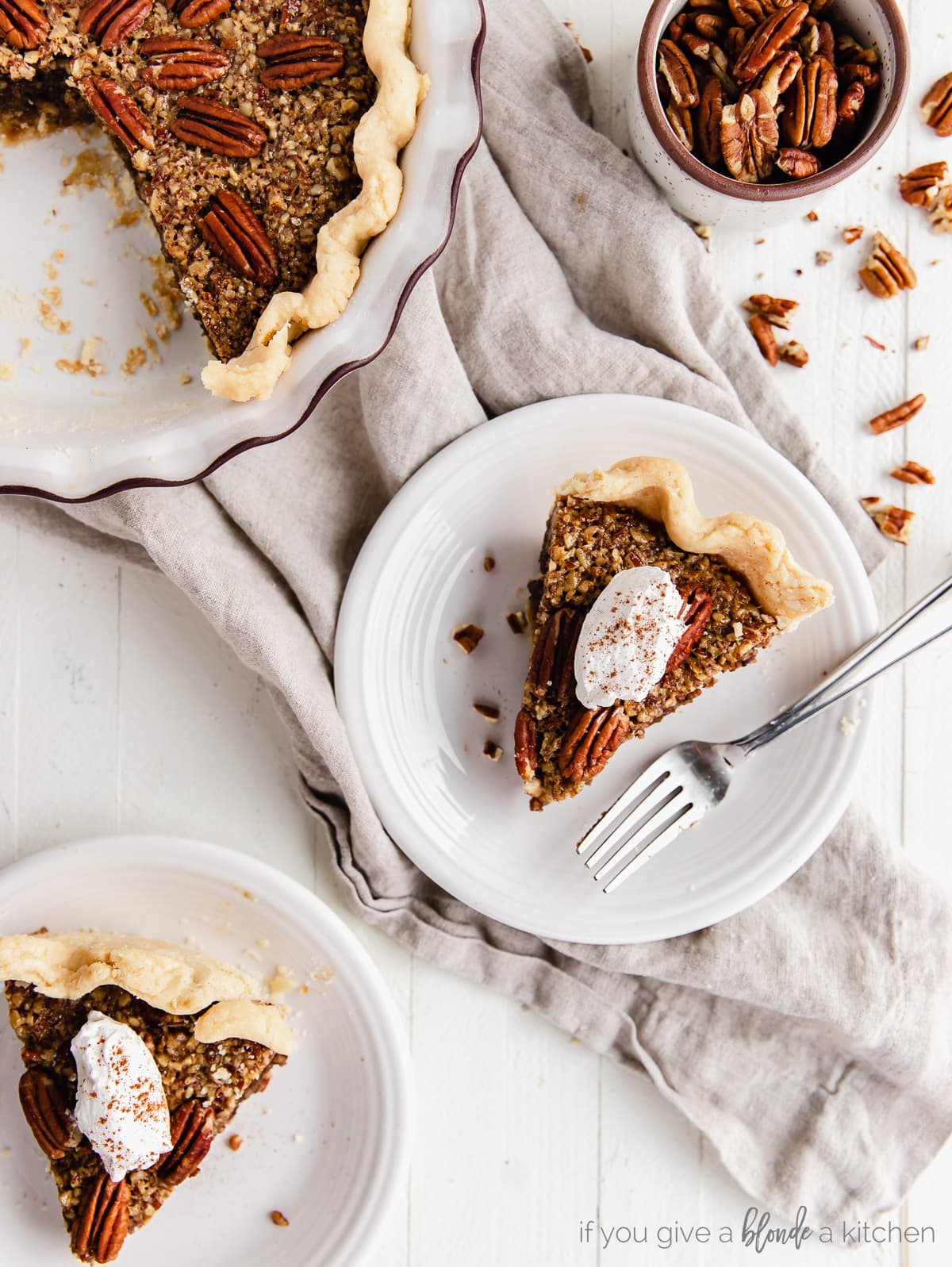 two slices of pecan pie with dollop of whipped cream on round white plates