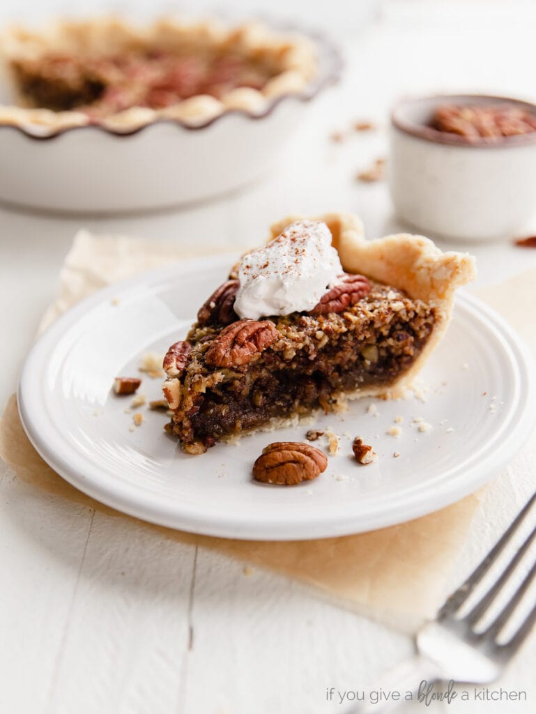 slice of pecan pie with dollop of whipped cream on round white plate