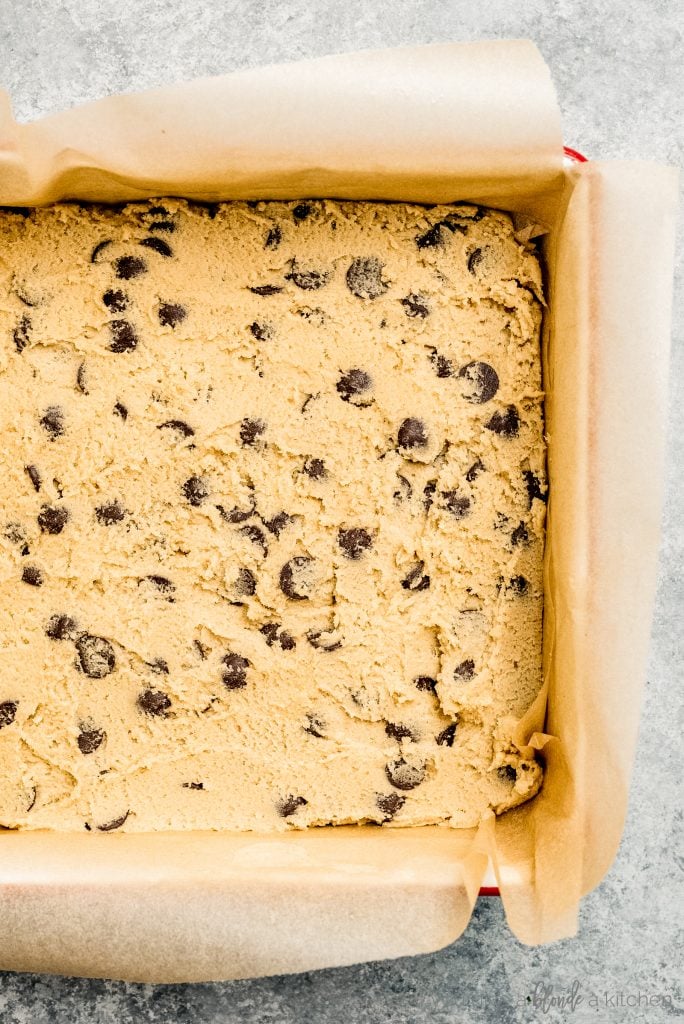 square baking pan with parchment paper and layer of cookie dough
