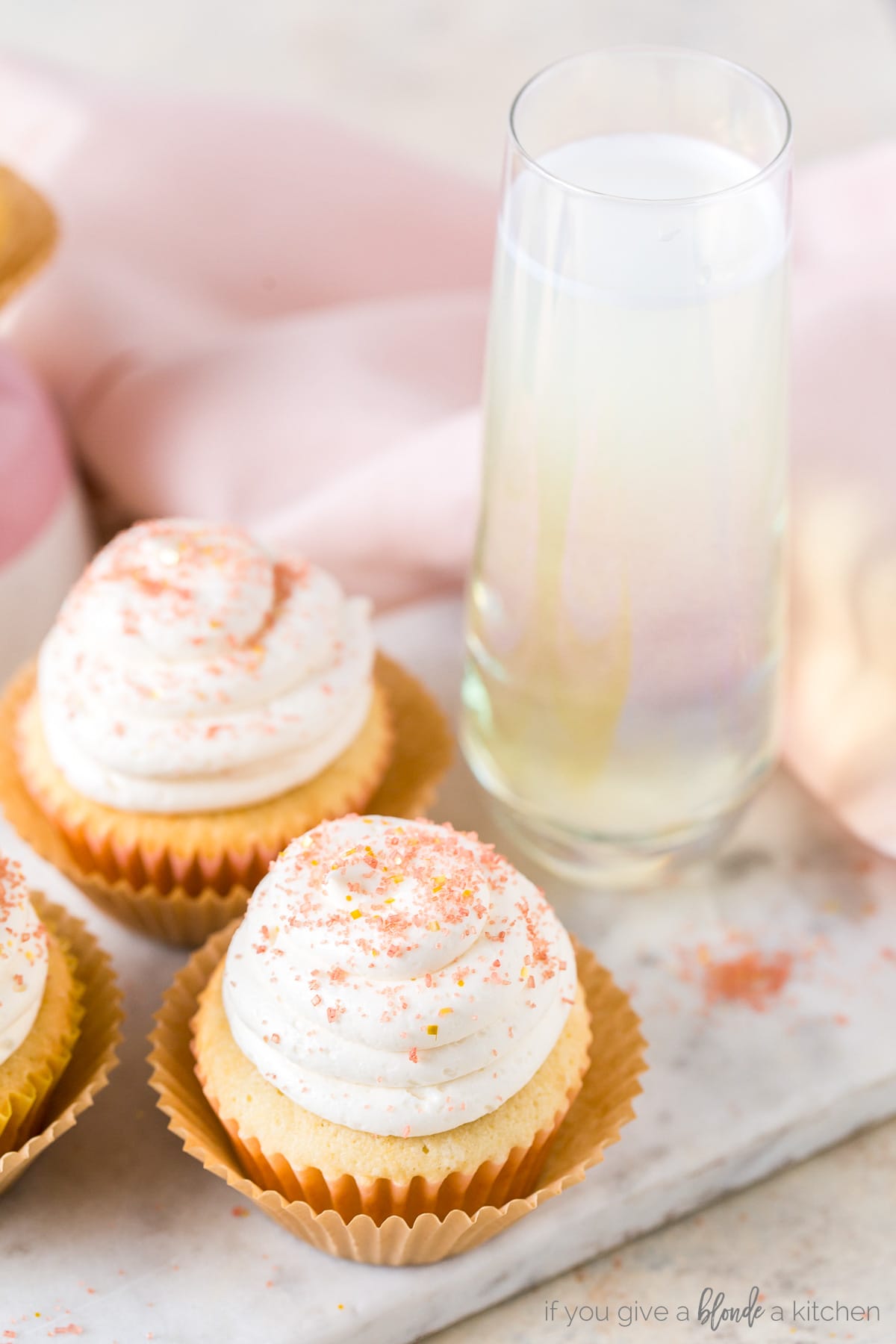champagne cupcakes with frosting and pink sprinkled next to stemless flute of champagne