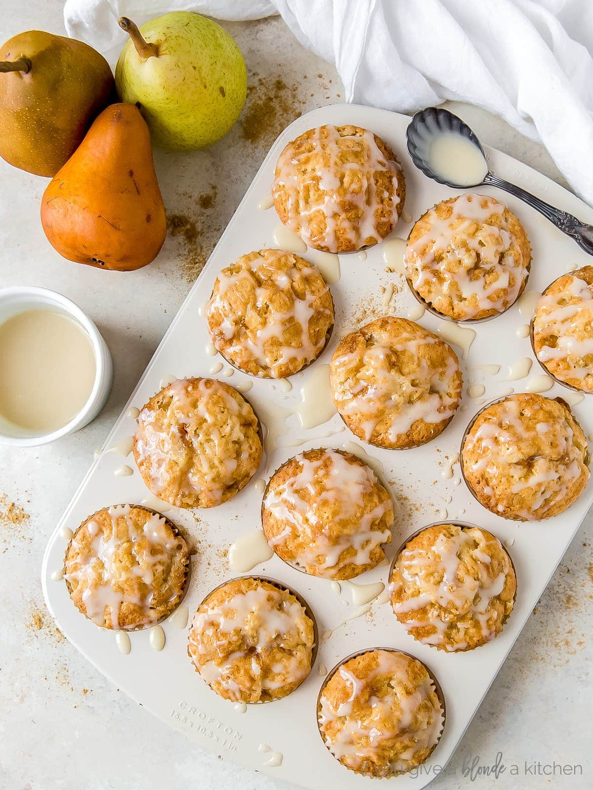 Glazed ginger pear muffins in a muffin tin; pears next to muffin tin.