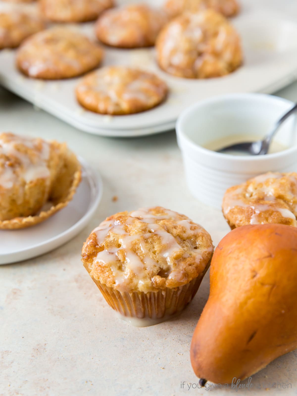 ginger pear muffin next to brown pear and bowl of honey glaze