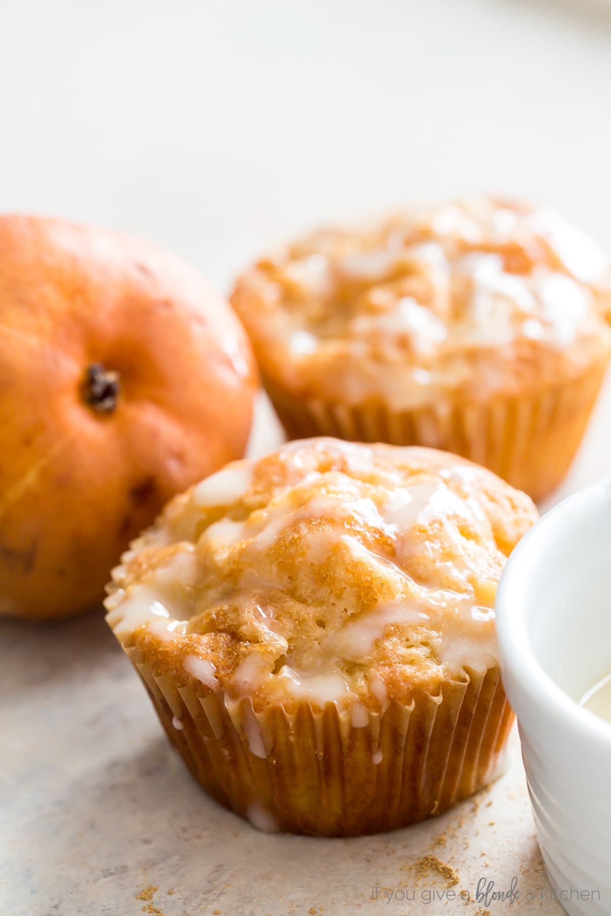 Two ginger pear muffins with glaze next to brown pear.