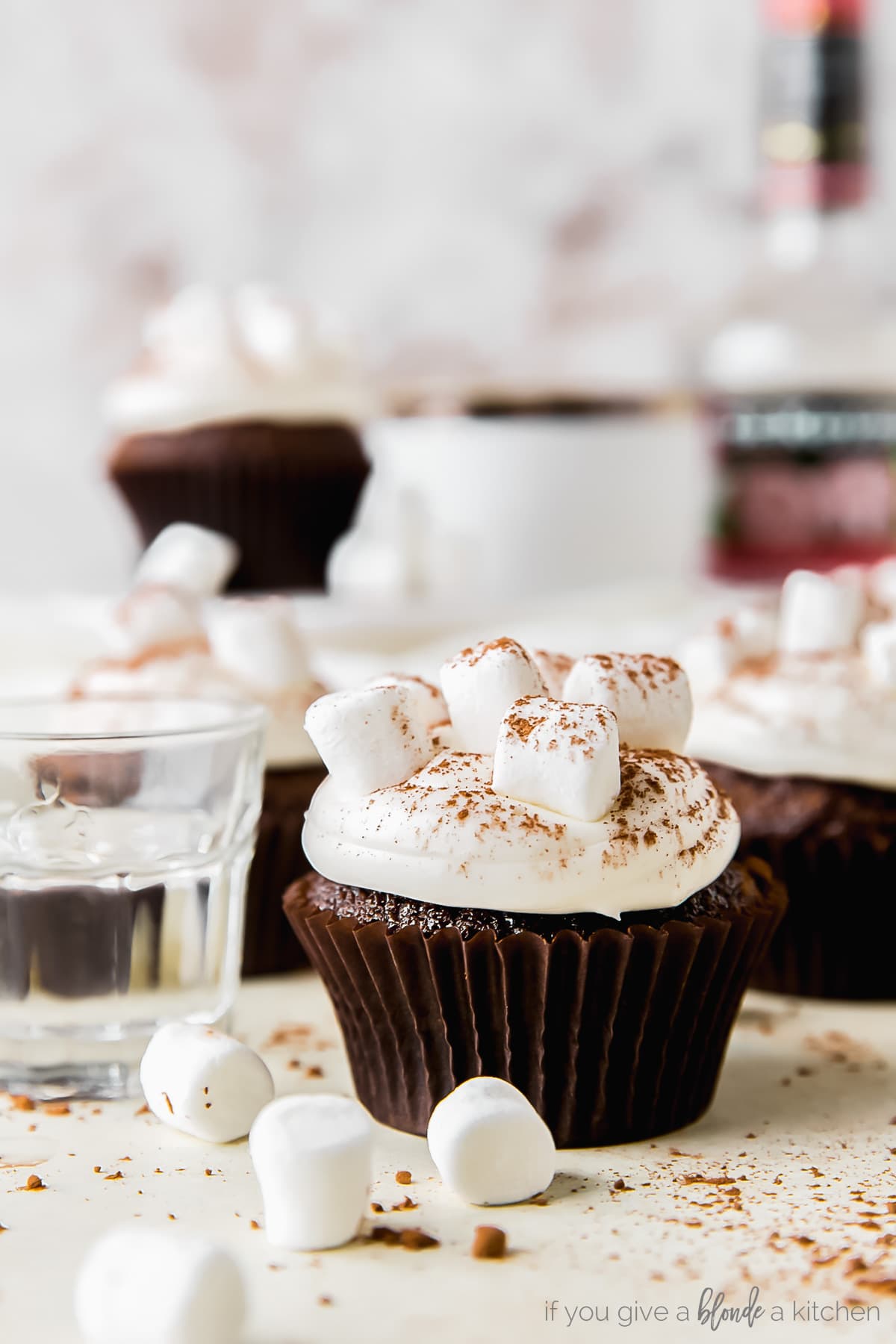 hot cocoa cupcake topped with marshmallow frosting, next to shot glass of peppermint schnapps