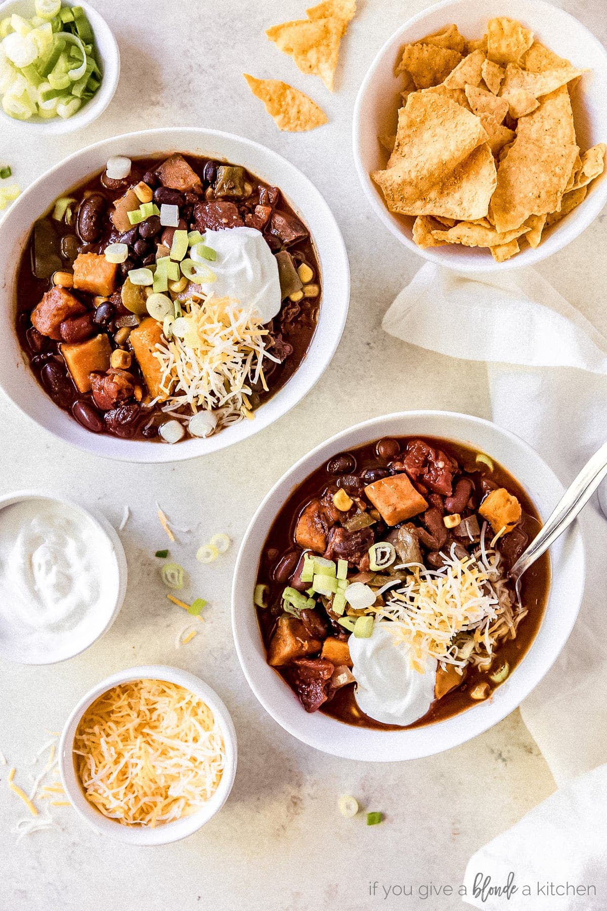 two bowls of sweet potato chili with sour cream, shredded cheese and green onion