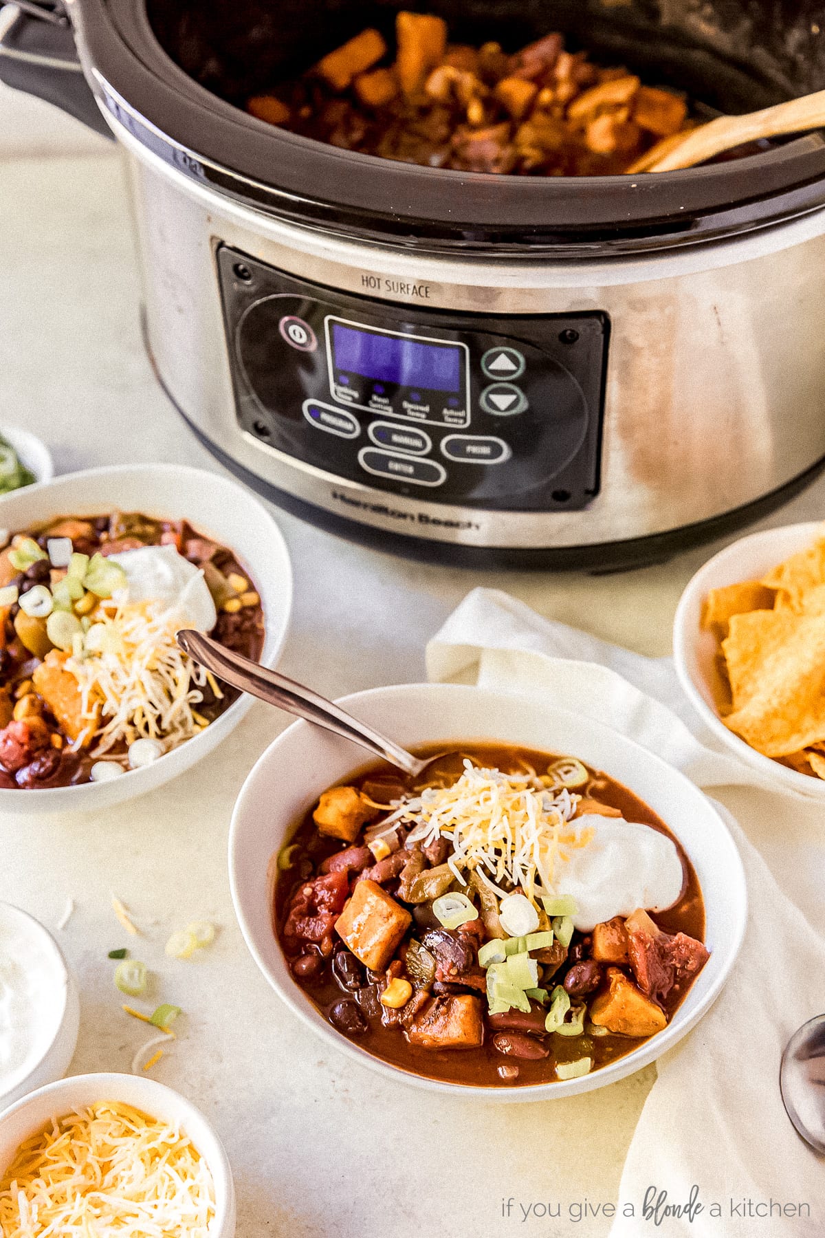 two bowls of sweet potato chili in front of stainless steel slow cooker full of chili
