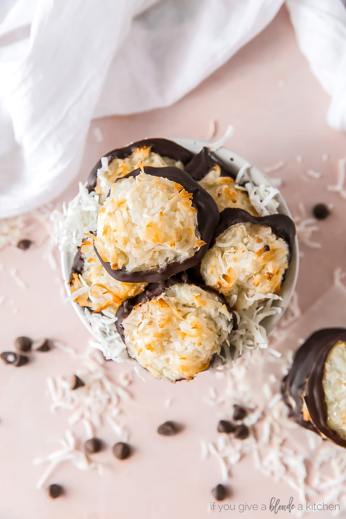 coconut macaroons piled in a small bowl with shredded coconut; bottoms of macaroons dipped in chocolate