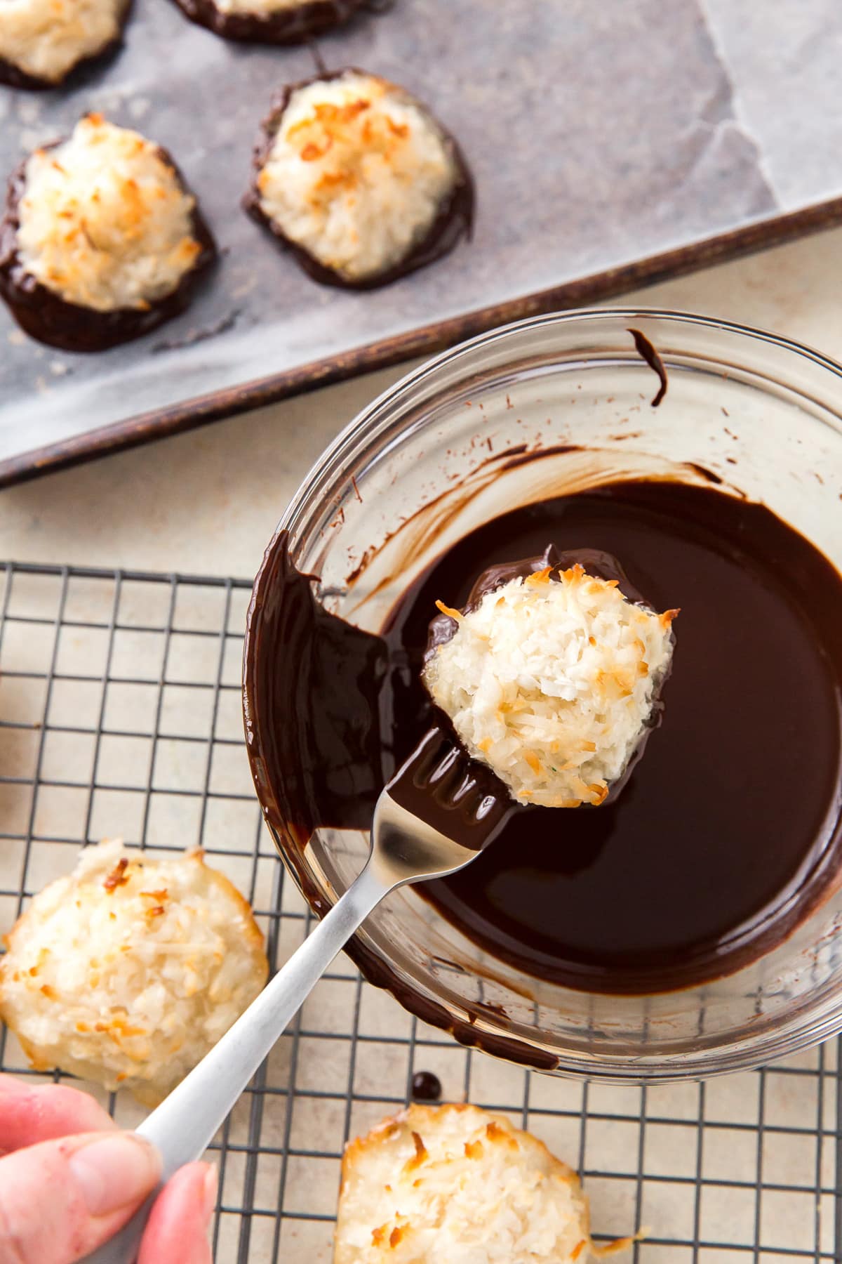 fork dipping coconut macaroon in bowl of melted chocolate