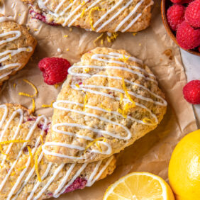 lemon raspberry scones on parchment paper with fresh raspberries and half a lemon.