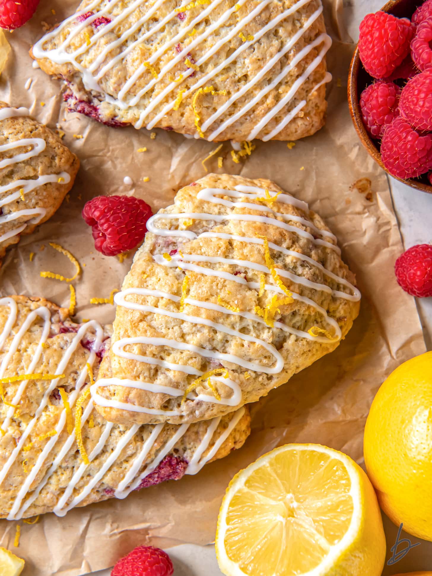 lemon raspberry scones on parchment paper with fresh raspberries and half a lemon.