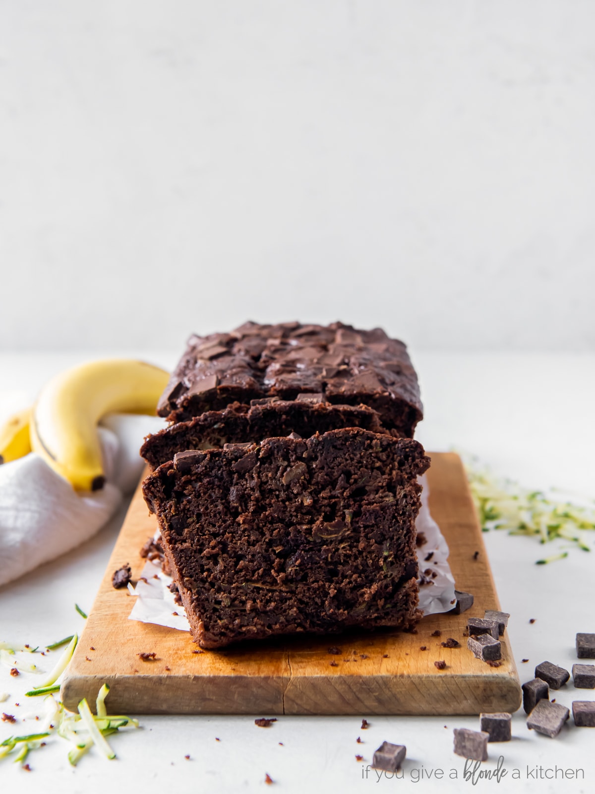 slices of chocolate zucchini banana bread leaning up against loaf on wood cutting board